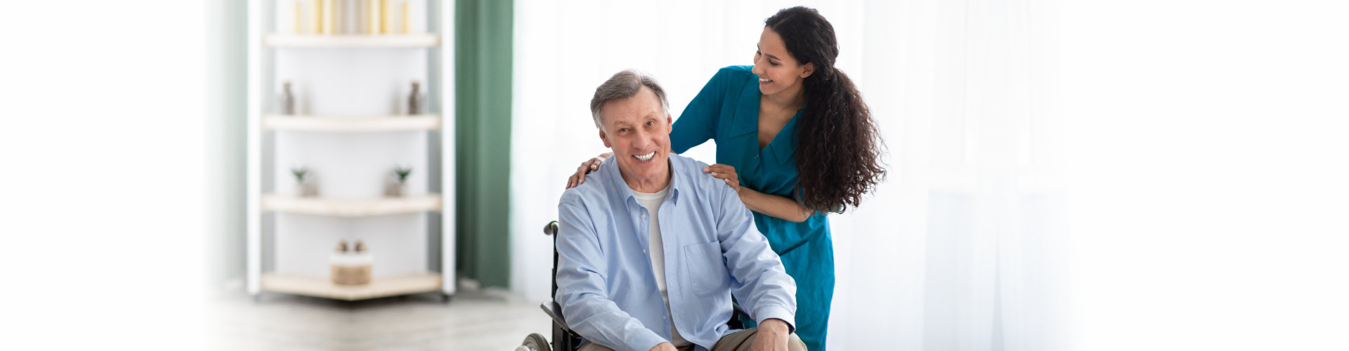 senior on a wheelchair and a woman caregiver smiling at him