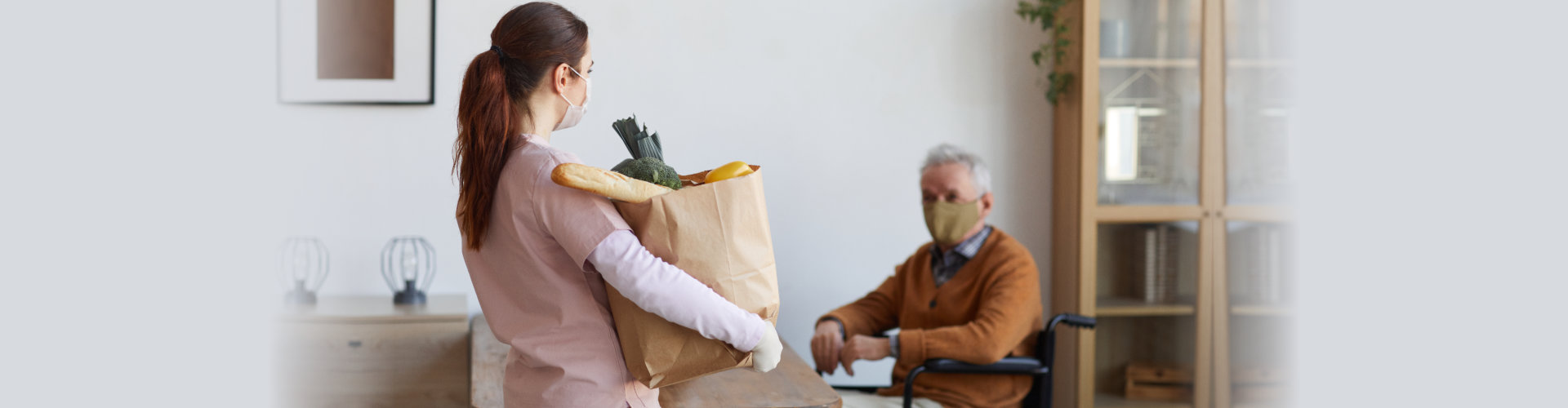 caregiver carrying groceries to a senior man on wheelchair