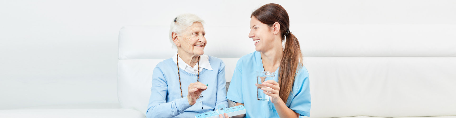 caregiver giving medicine to a senior woman smiling at each other